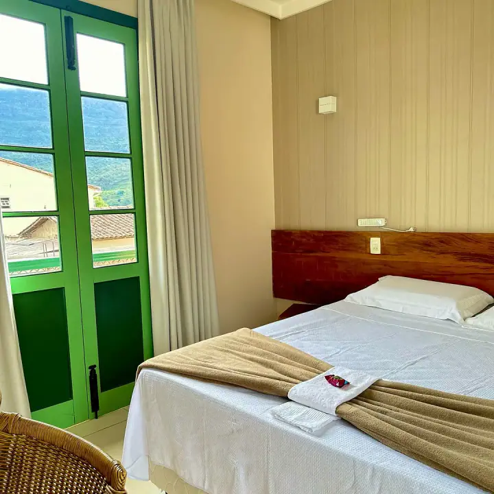 Acomodação com cama de madeira, porta verde e vista da serra