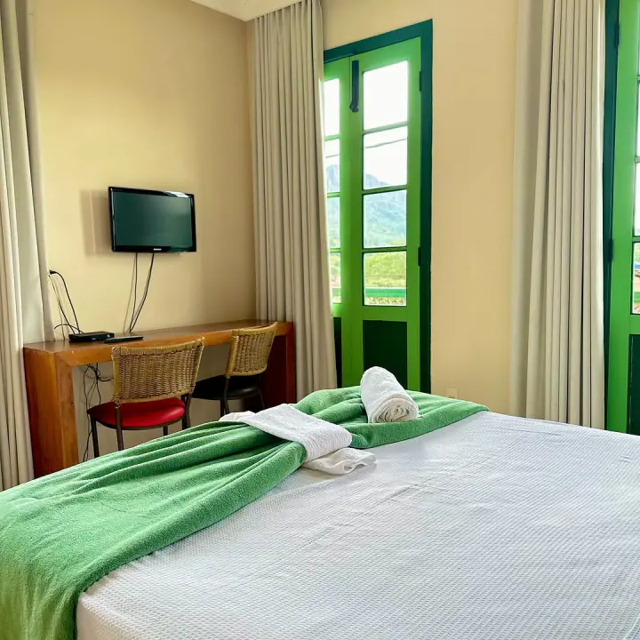 Quarto com roupa de cama branca e esquadrias verdes